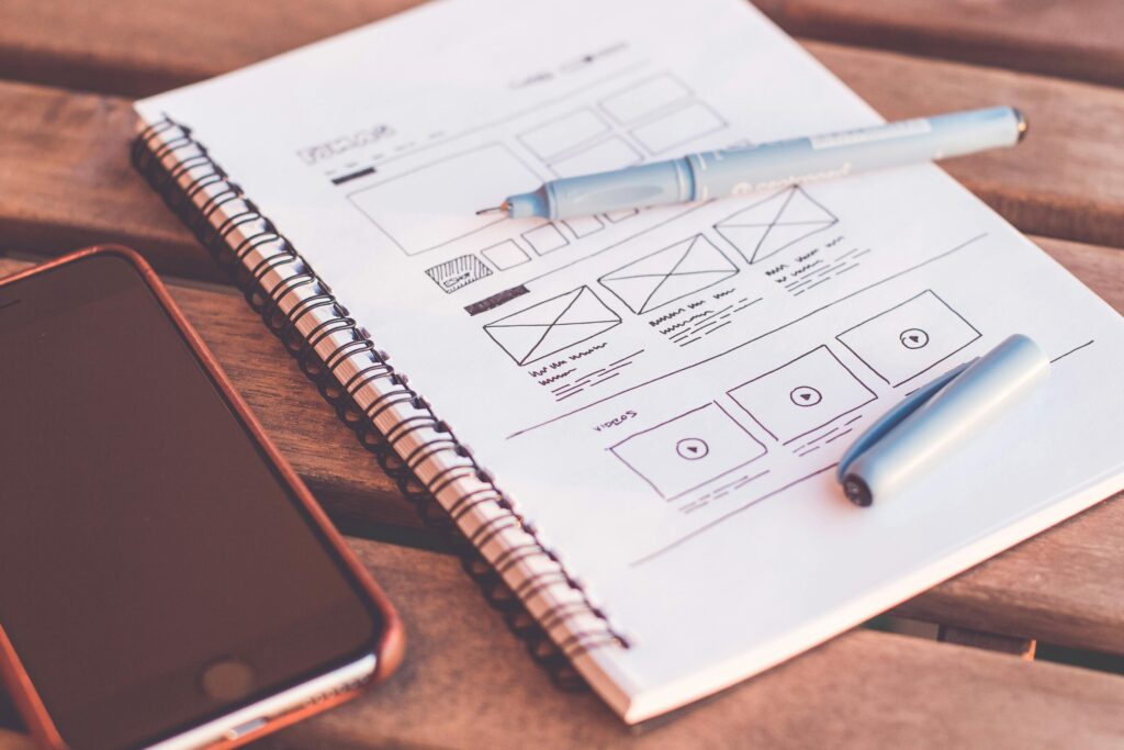 pexels photo 196644 196644 Close-up of a notebook with wireframe sketches and a smartphone on a wooden desk.